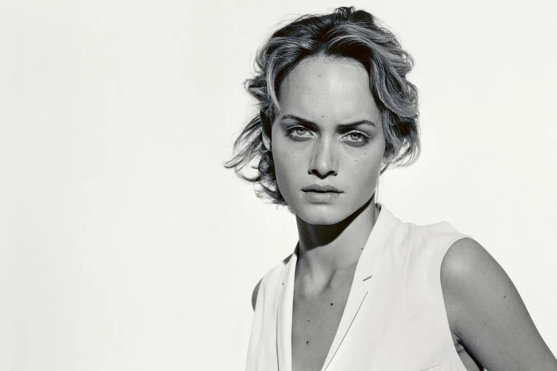 Black-and-white portrait of a woman with short, wavy hair wearing a sleeveless white top, looking directly at the camera with a serious expression.