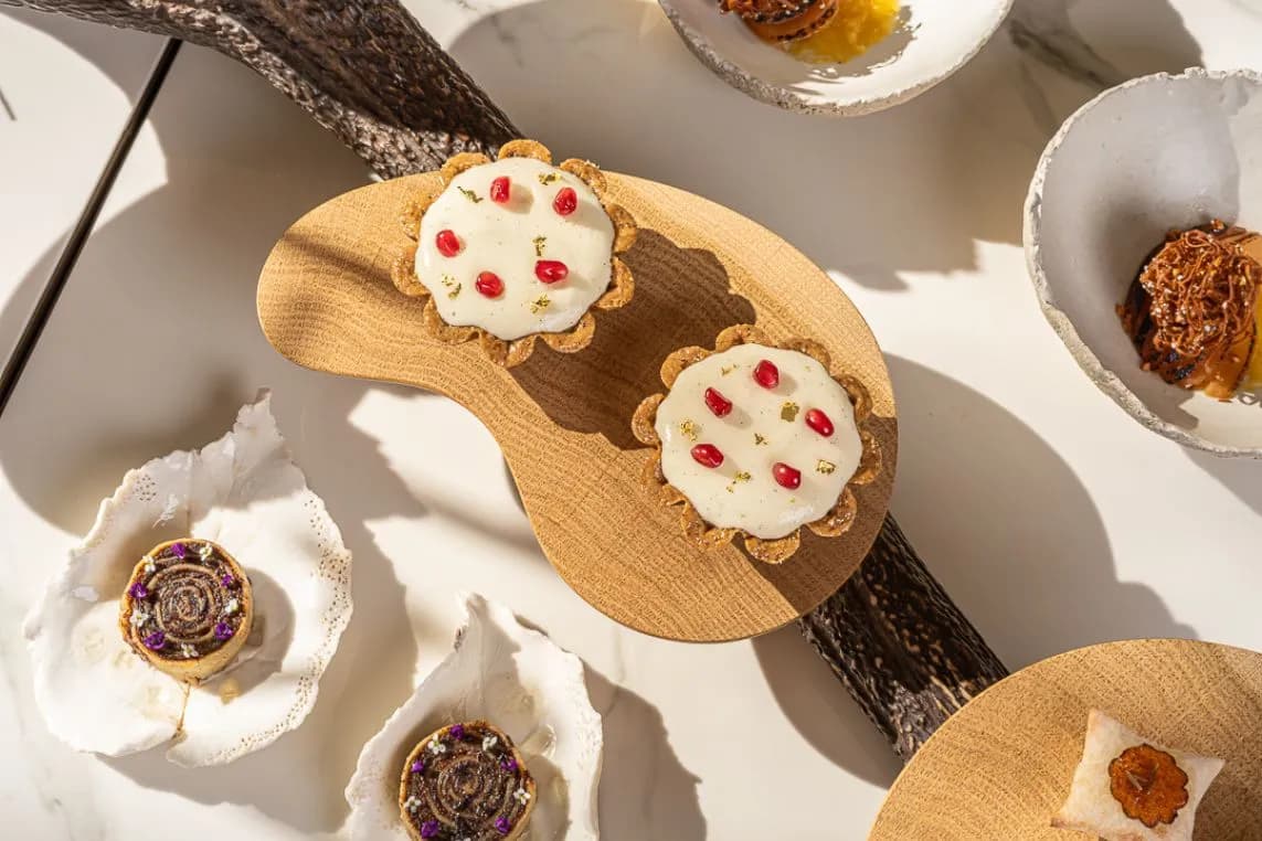 Two round cookies with white icing and red sprinkles on a wooden board, surrounded by decorative shells and assorted treats.