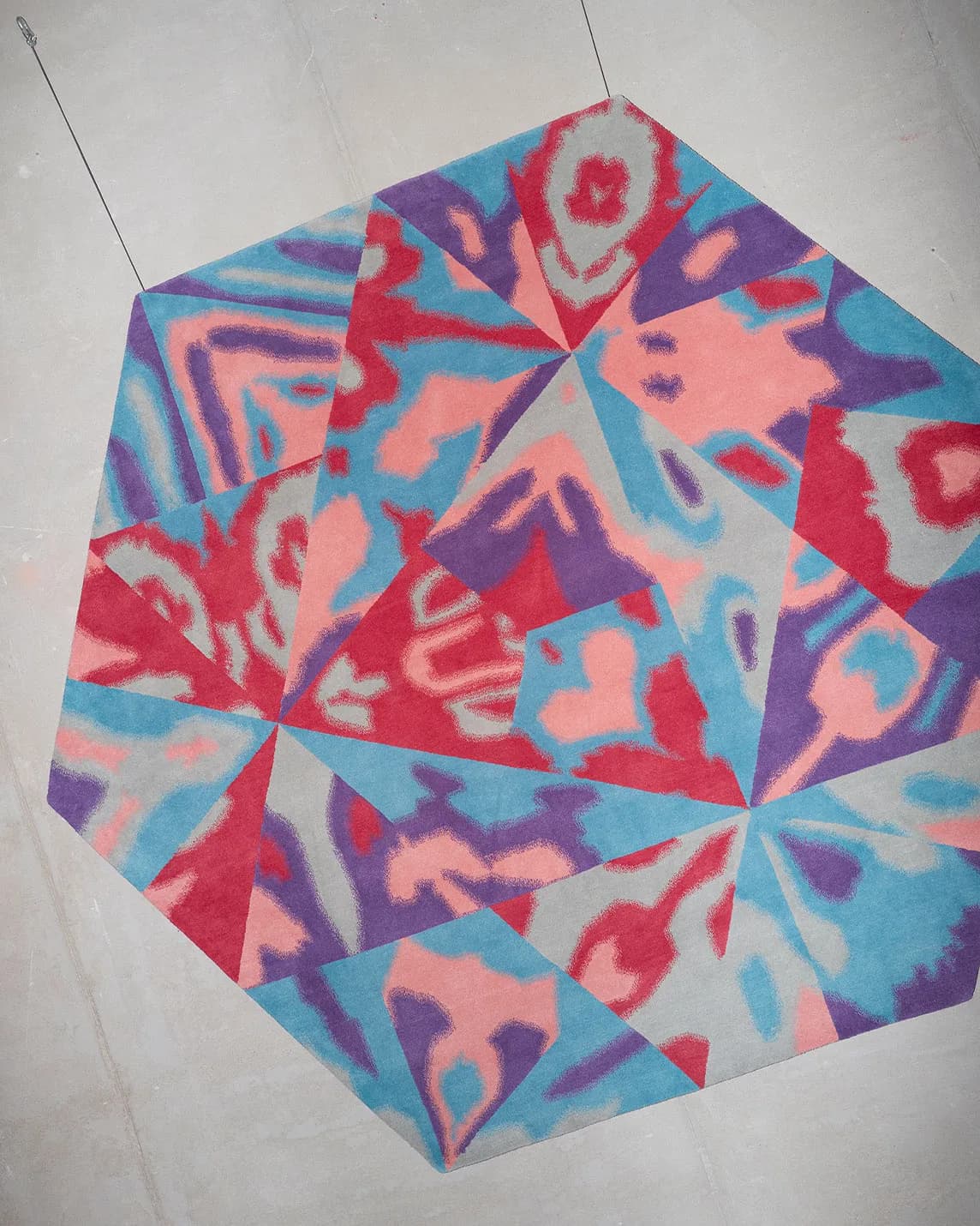 Colorful tie-dye quilt laid on the floor, featuring a circular patchwork of red, pink, blue and purple triangles in a star-like pattern.