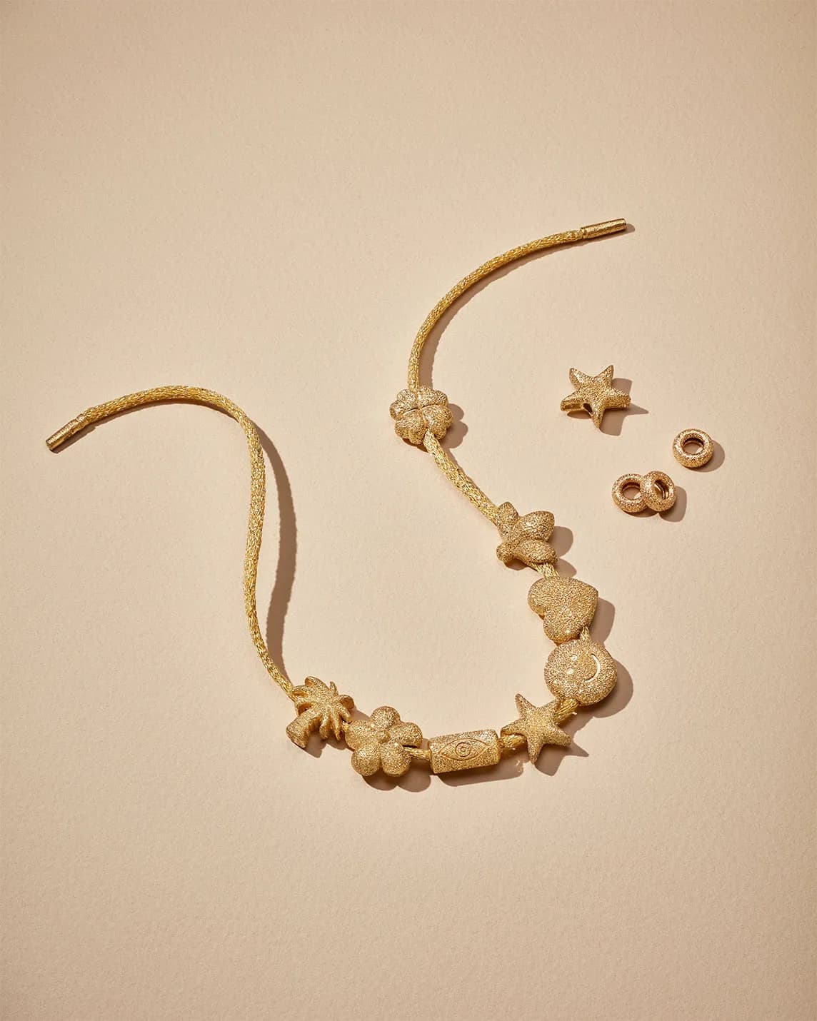 Gold-tone charm necklace with starfish, flowers and heart beads laid on a beige background, with matching loose charms nearby.