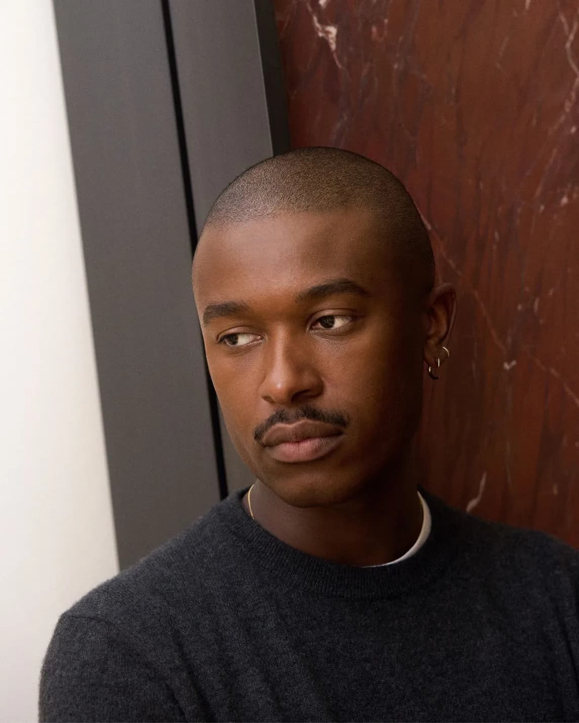 Portrait of a man with a shaved head and mustache, wearing a dark sweater, gazing to his left.