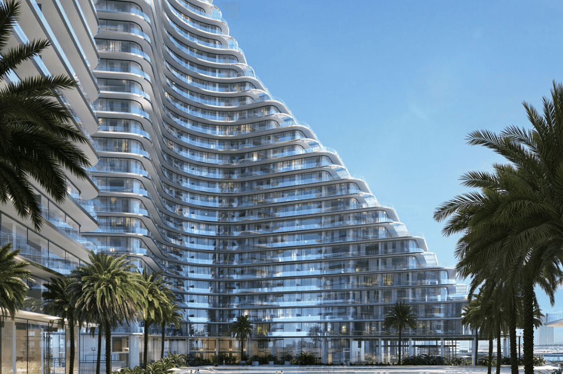 Daytime view of Binghatti Flare showing curved residential towers overlooking a large pool deck with sun loungers, seating areas, landscaped greenery, and surrounding palm trees.