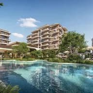 Modern resort with a large swimming pool, loungers and umbrellas, surrounded by multi-story beige buildings and lush greenery.