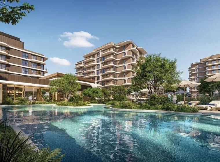 Modern resort with a large swimming pool, loungers and umbrellas, surrounded by multi-story beige buildings and lush greenery.