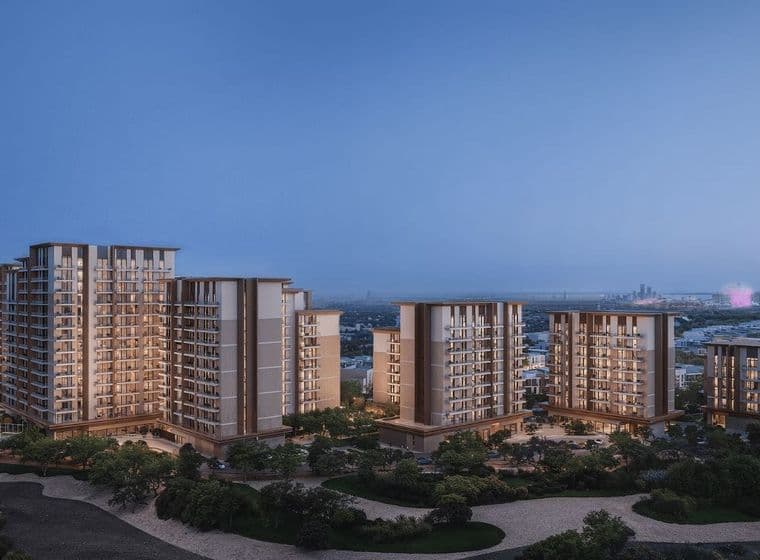 A cluster of modern high-rise residential buildings at dusk, surrounded by greenery with a city skyline in the distant background.