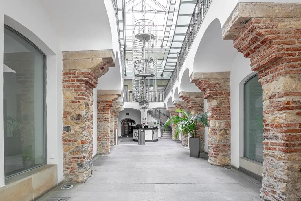 Bright atrium with stone and brick columns, a glass roof and a metal spiral staircase.