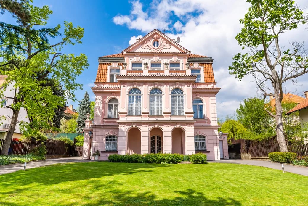 Pink historic villa with an ornate façade, tiled roof and well-maintained green garden.