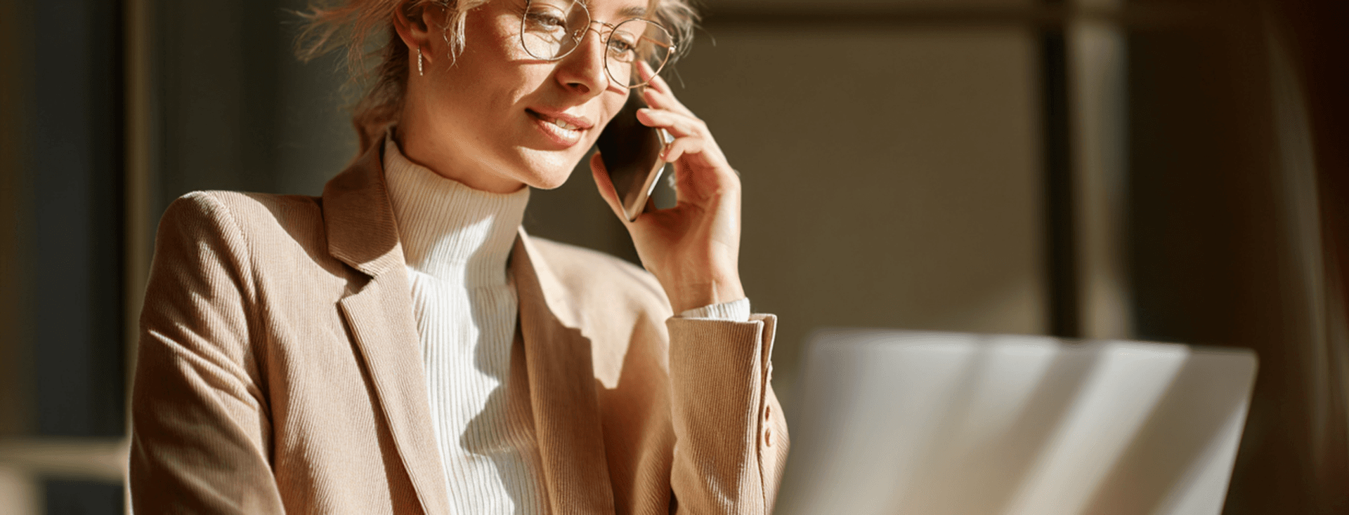 Woman talking on the phone, in front of a laptop, under direct sunlight.
