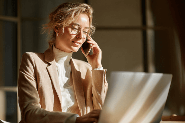 Woman talking on the phone, in front of a laptop, under direct sunlight.