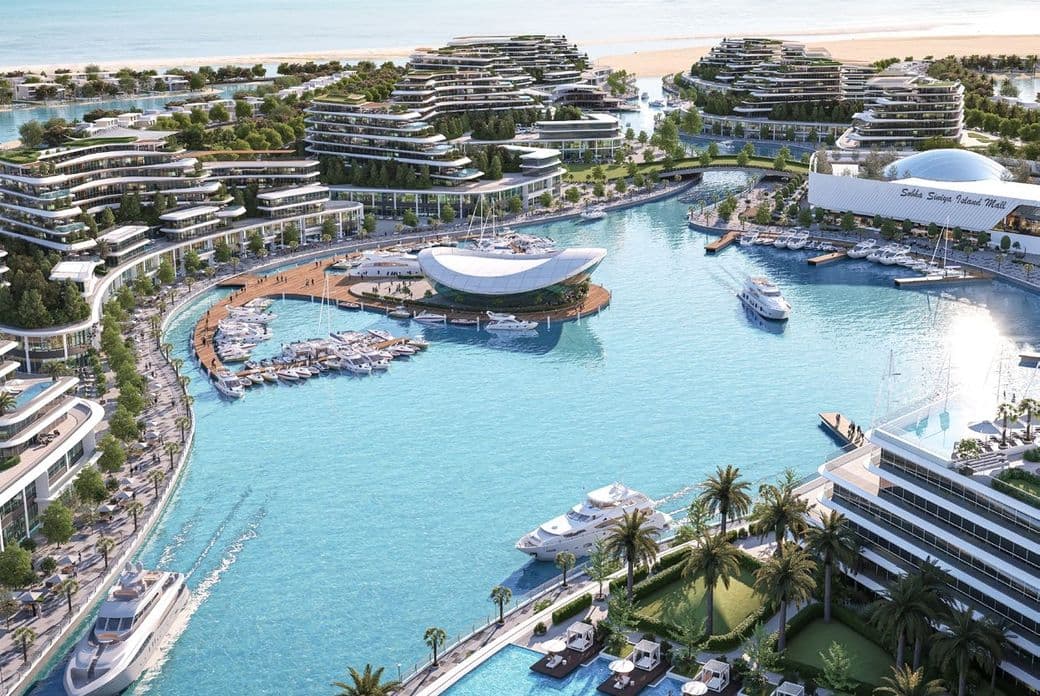 Futuristic waterfront development with modern buildings, yachts docked in a marina, and lush greenery lining the shoreline.
