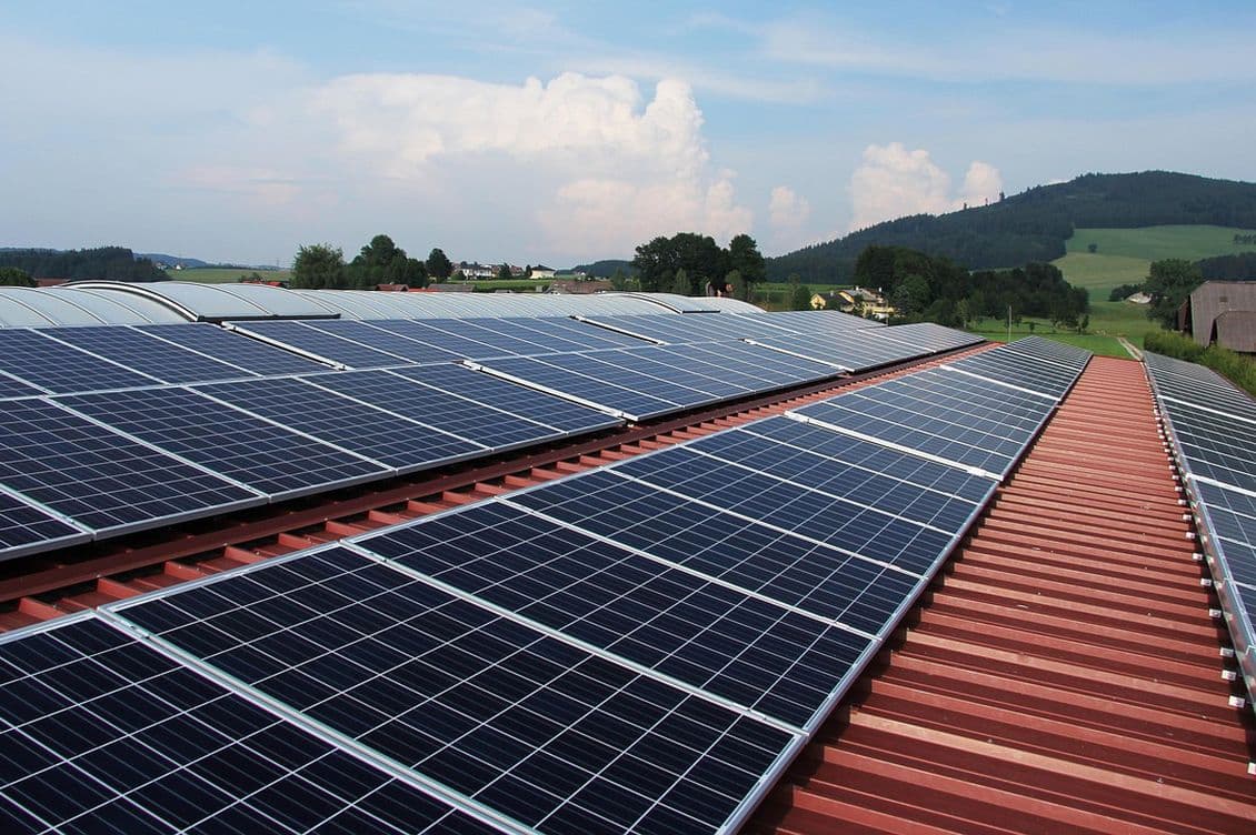 View over the roof of a commercial building with solar panels in a green, hilly landscape.
