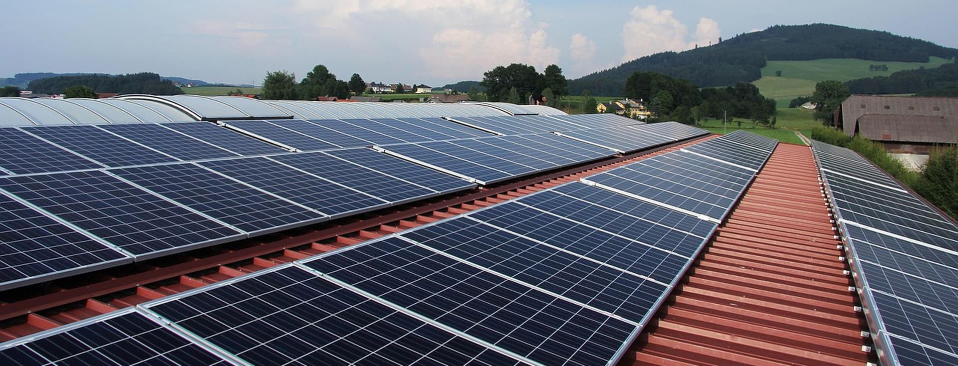 View over the roof of a commercial building with solar panels in a green, hilly landscape.