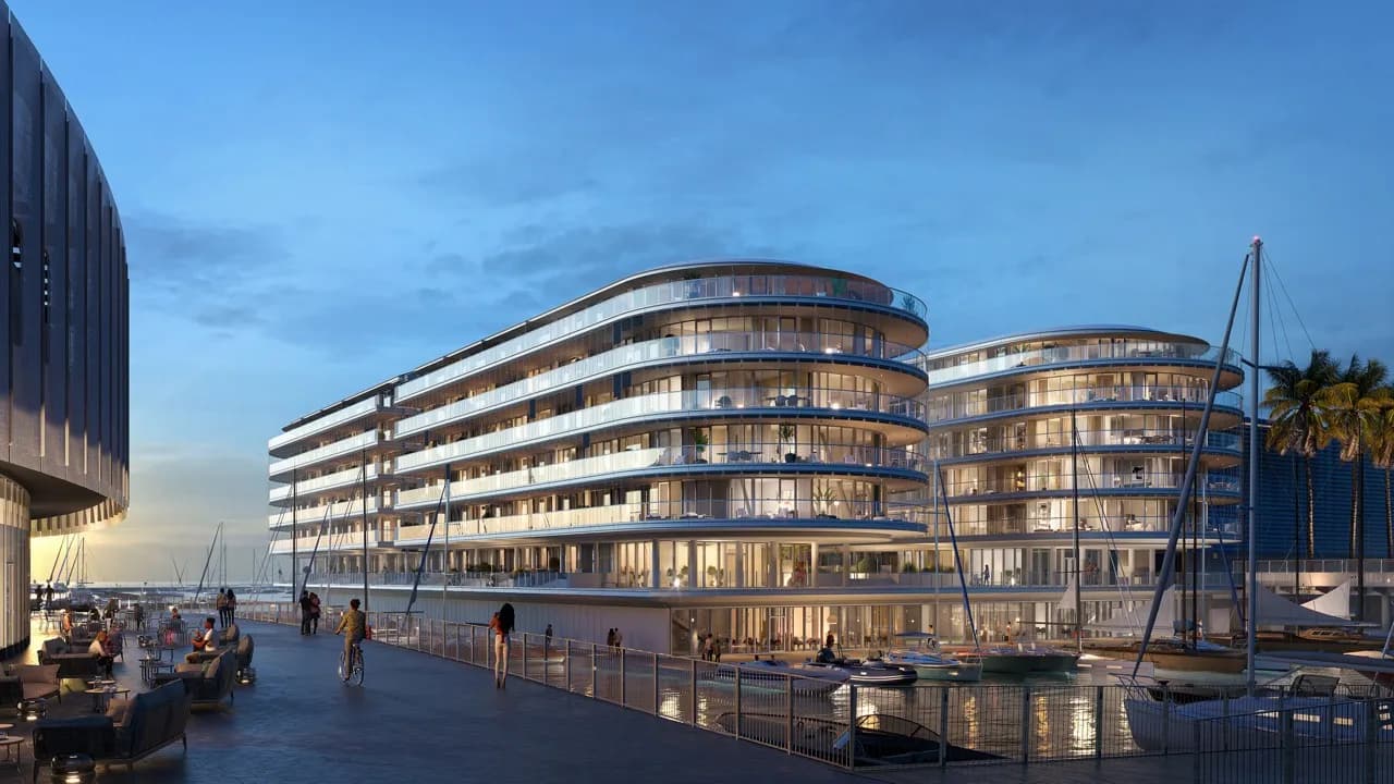 Futuristic waterfront buildings with curved glass façades at sunset, surrounded by boats and palm trees, beneath a clear blue sky.