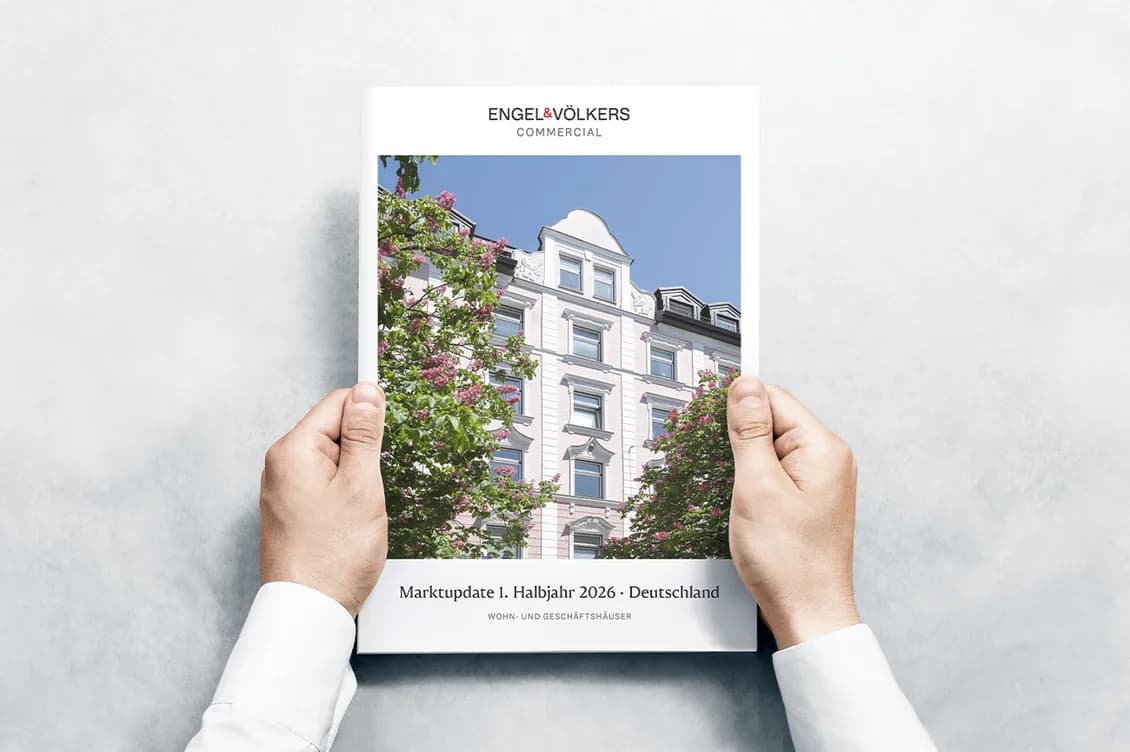Zwei Hände halten den Marktbericht für Wohn- und Geschäftshäuser in Deutschland (1. Halbjahr 2026); auf dem Cover steht „Engel & Völkers Commercial“.