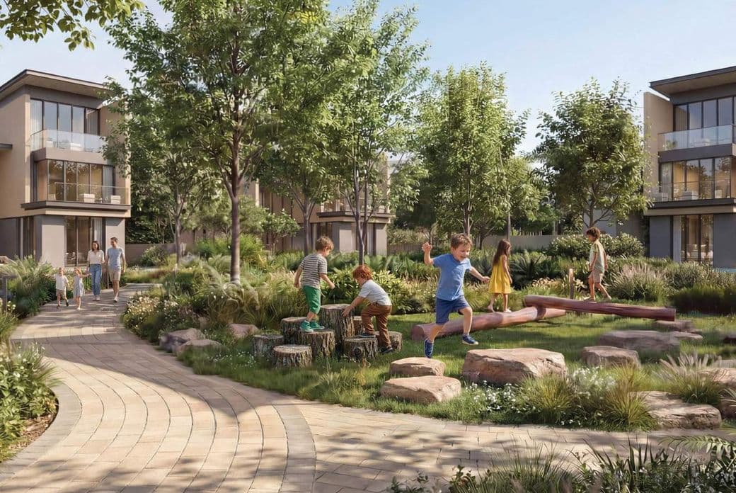 Children play on logs and rocks in a lush garden surrounded by modern houses, while a family walks along a curved brick path.