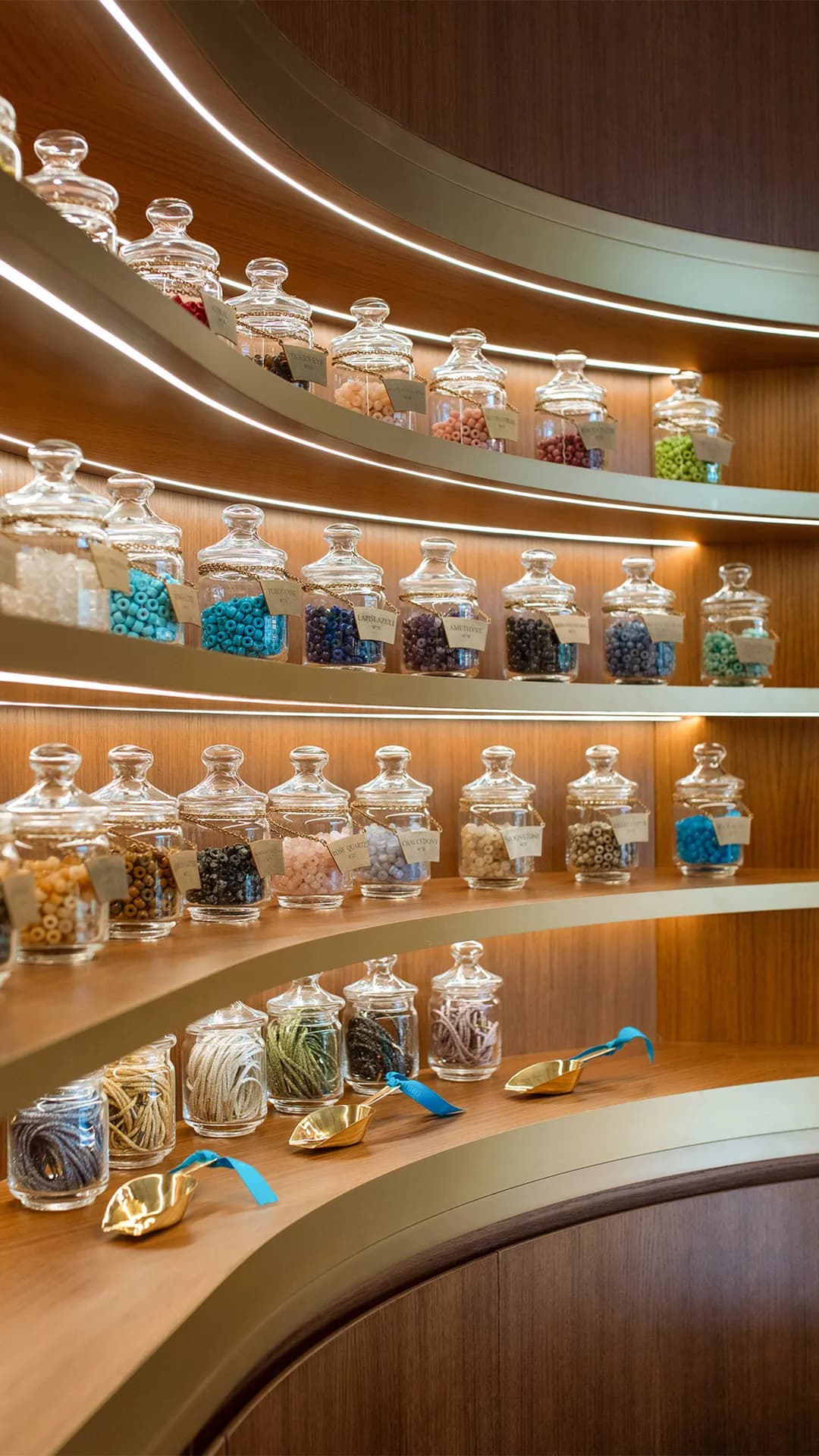 Curved wooden shelves lined with glass apothecary jars with lids, filled with colorful beads and candies under warm lighting.