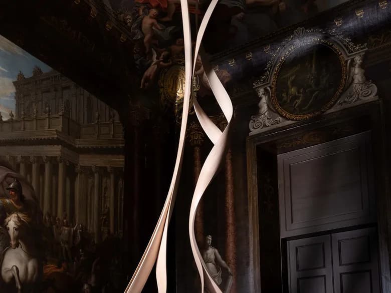 A sumptuous room with a painted ceiling; a delicate, ribbon-like sculpture rises from a bed draped in white, set amidst dark wood panelling and classic furnishings.