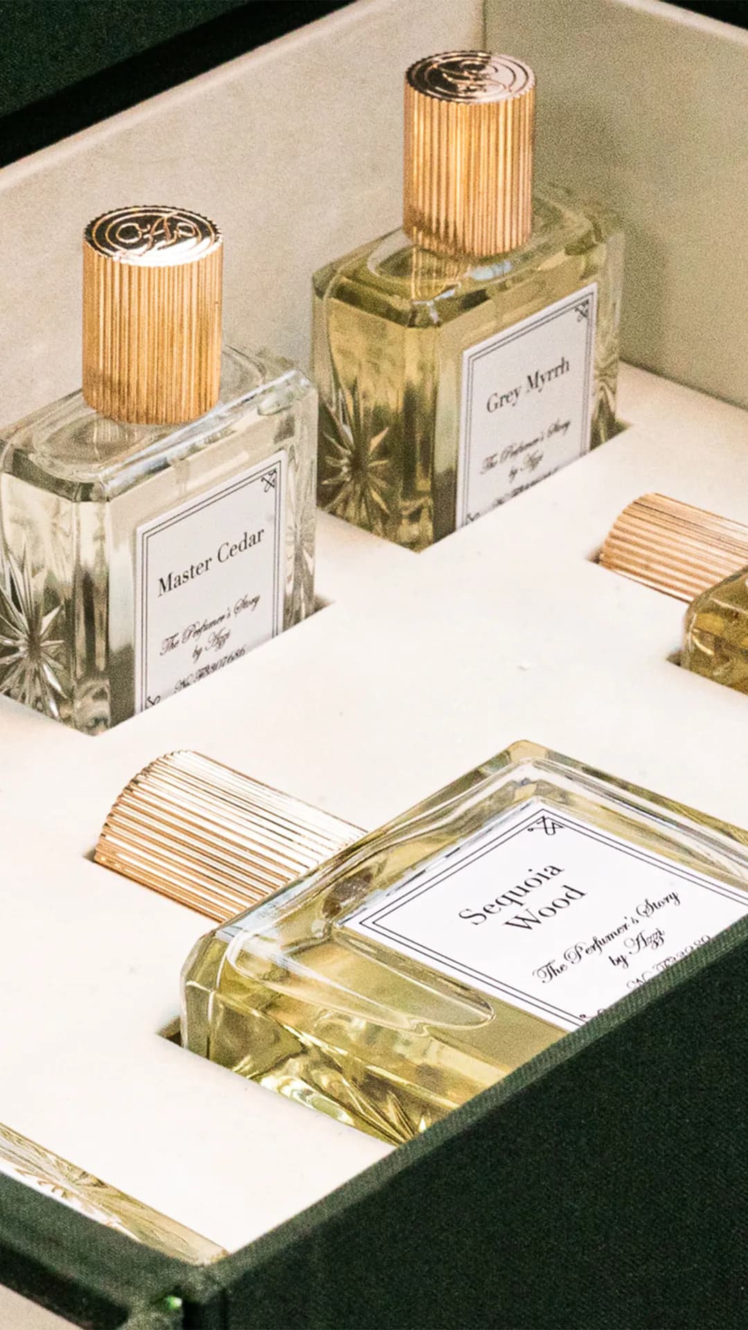 Row of glass perfume bottles with fluted gold stoppers in a display case; the labels read Master Cedar, Gray Myrrh, After Hours.