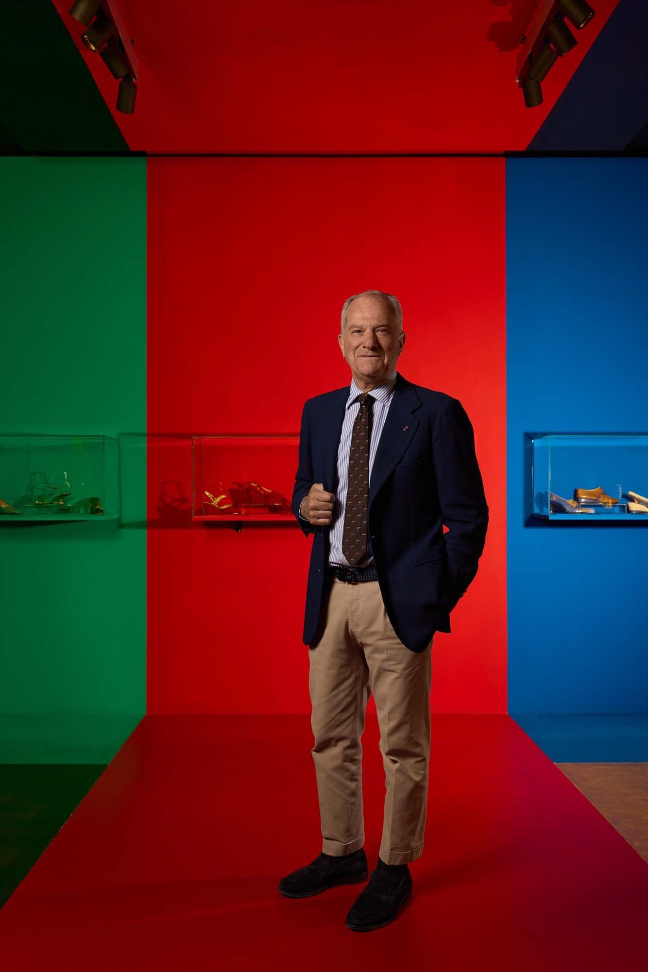 A man in a suit stands in a colourful room with red, green and blue walls, where various objects are displayed in glass cases.