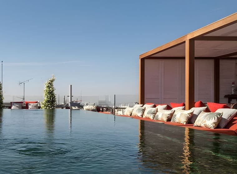 Piscina infinita en la azotea con zona de descanso, cojines rojos y cielo despejado de fondo. Un entorno elegante y sereno.