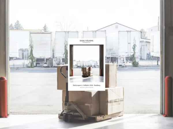 Loading dock with a pallet of boxes in the foreground; a centered poster for Engel & Völkers Commercial shows a warehouse image.