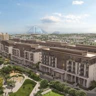 Aerial view of a modern residential complex with landscaped gardens, pathways, and distant city landmarks under a partly cloudy sky.