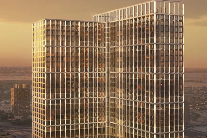 Two glass-clad office towers connected by a sky bridge, bathed in sunset light with warm reflections on grid-like windows.