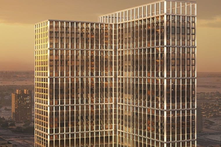 Two glass-clad office towers connected by a sky bridge, bathed in sunset light with warm reflections on grid-like windows.