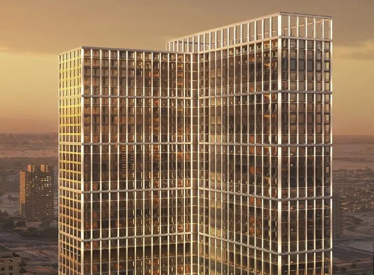 Two glass-clad office towers connected by a sky bridge, bathed in sunset light with warm reflections on grid-like windows.
