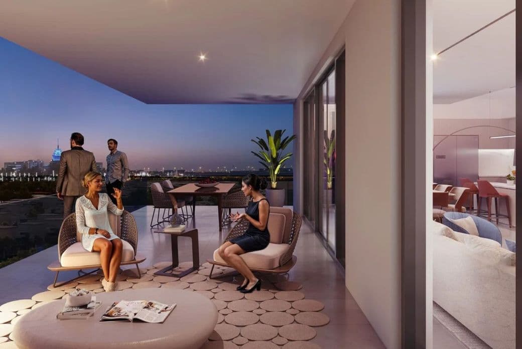 People socializing on a modern terrace at dusk, with a cityscape in the background and a stylish indoor area visible through glass doors.