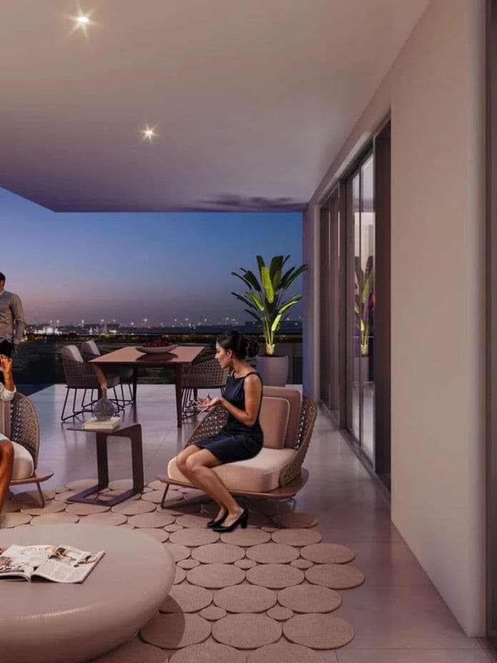 People socializing on a modern terrace at dusk, with a cityscape in the background and a stylish indoor area visible through glass doors.