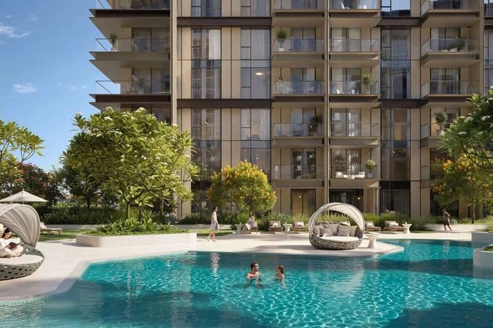 Modern apartment building with glass balconies, trees, and a pool. People are swimming and relaxing around the pool on a sunny day.