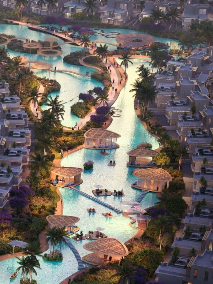 Aerial view of a luxurious resort with winding pools, palm trees, loungers, and modern villas during sunset.