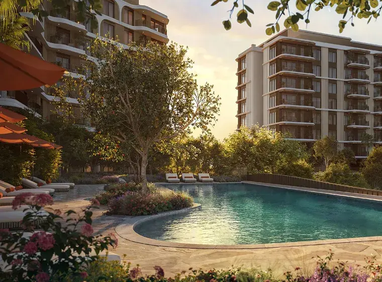 Sunset over a resort-style apartment complex with a curved turquoise pool, lounge chairs, and modern high-rise buildings.