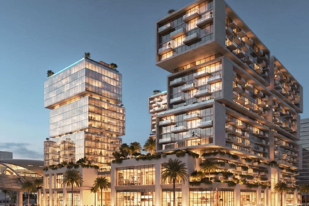 Modern, illuminated building complex with stacked glass structures, surrounded by palm trees at dusk, with people and cars in the foreground.
