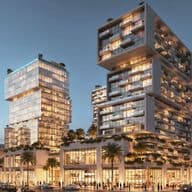 Modern, illuminated building complex with stacked glass structures, surrounded by palm trees at dusk, with people and cars in the foreground.