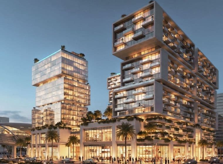 Modern, illuminated building complex with stacked glass structures, surrounded by palm trees at dusk, with people and cars in the foreground.
