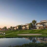 Golf course with two players near a sand trap, modern houses, and palm trees in the background under a clear blue sky.
