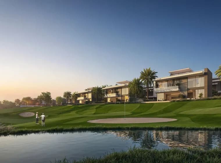Golf course with two players near a sand trap, modern houses, and palm trees in the background under a clear blue sky.