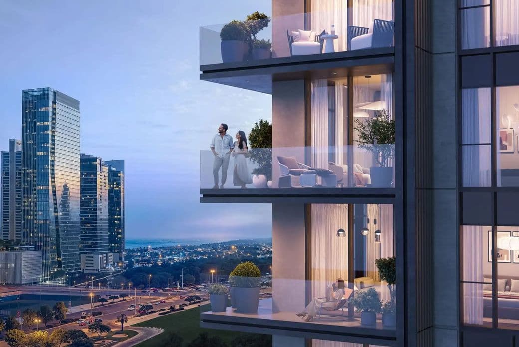 Couple standing on a modern high-rise balcony at dusk, city skyline in background, with warm interior lights and a seated couple on a lower balcony.