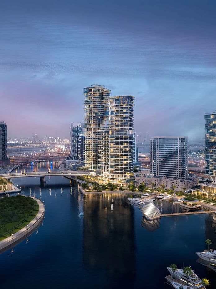 Aerial view of a modern waterfront cityscape at dusk, with high-rise buildings, lush greenery, boats, and a serene waterway reflecting lights.