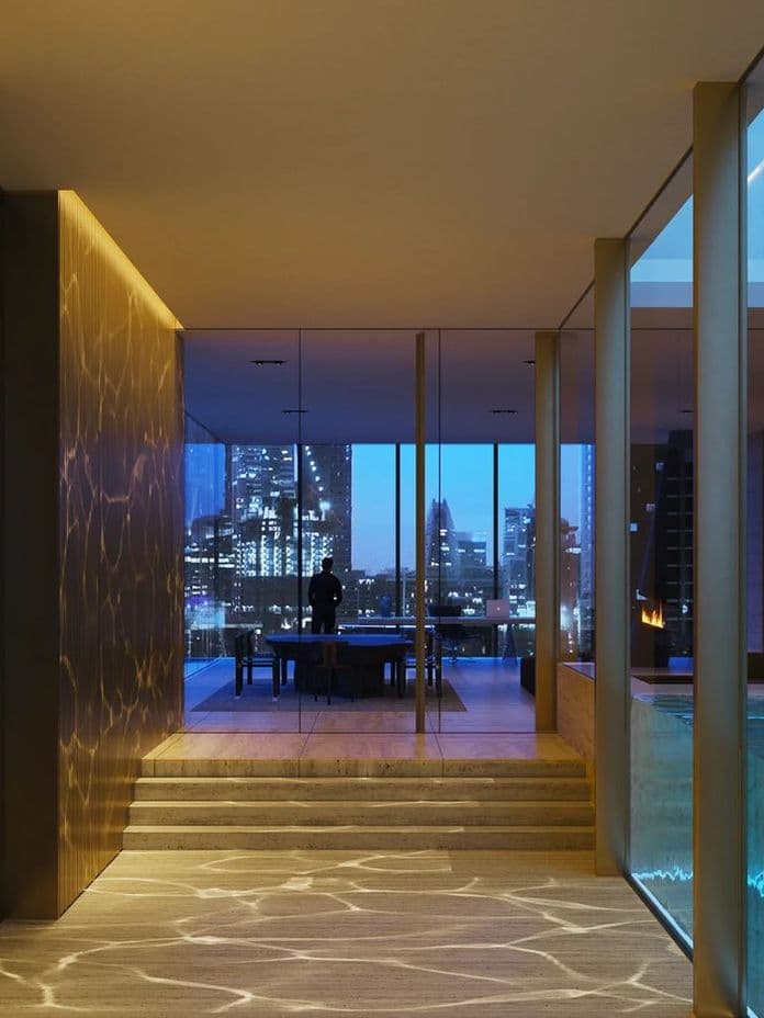 Modern interior with warm lighting, glass walls, and a view of a city skyline at night. Features a pool and a seating area.