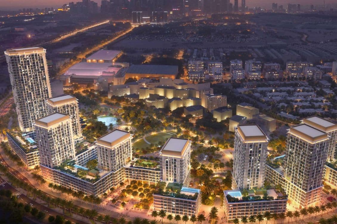 Aerial dusk view of illuminated apartment towers with rooftop pools and a distant city skyline