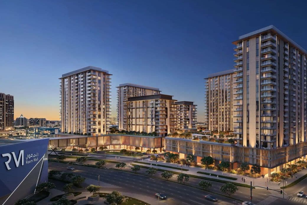 Modern cityscape at dusk featuring illuminated high-rise buildings, a busy road, and trees, with a prominent building on the left side.