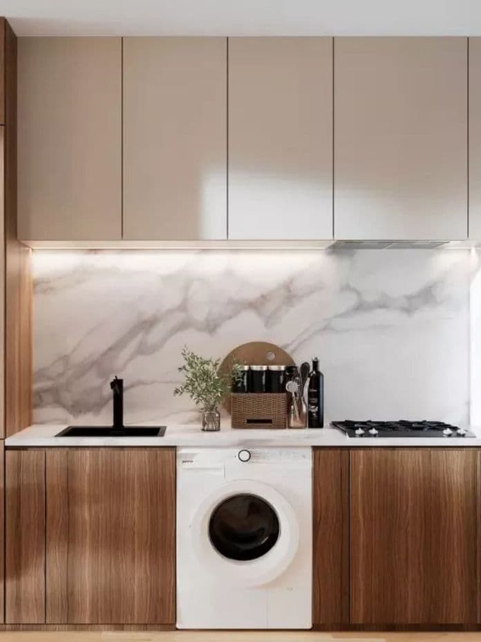 Modern kitchen with wooden cabinets, marble backsplash, washing machine, black sink, stovetop, and a basket with plants on the counter.