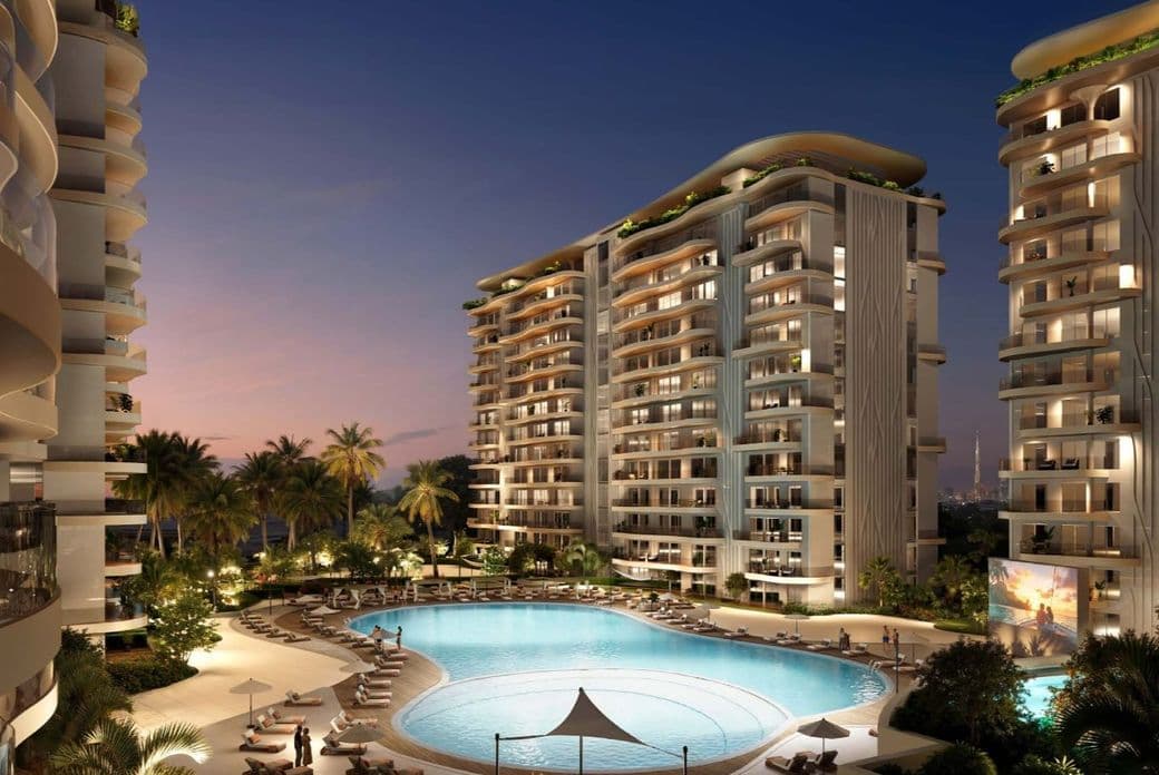 Luxurious residential complex at dusk with illuminated high-rise buildings, a large pool, palm trees, and people relaxing by lounge chairs.