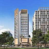 Modern high-rise building with a sleek design, flanked by trees and surrounded by urban structures under a clear blue sky.