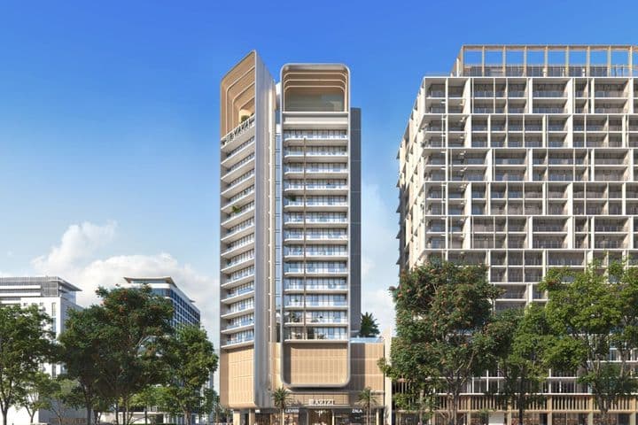 Modern high-rise building with a sleek design, flanked by trees and surrounded by urban structures under a clear blue sky.