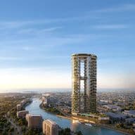Two circular towers linked by a sky bridge, covered in greenery, rising beside a winding canal with boats and a distant city under a blue sky.