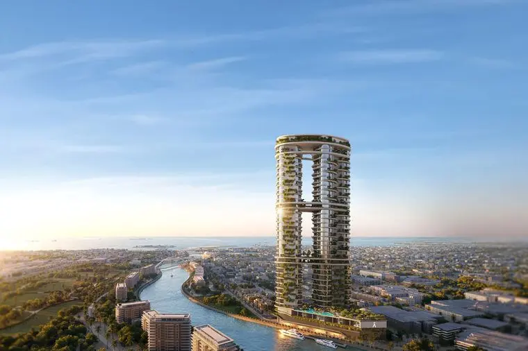 Two circular towers linked by a sky bridge, covered in greenery, rising beside a winding canal with boats and a distant city under a blue sky.